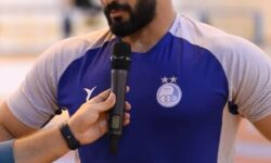 حسن یزدانی با پیراهن آبی روی تشک کشتی می‌رود
